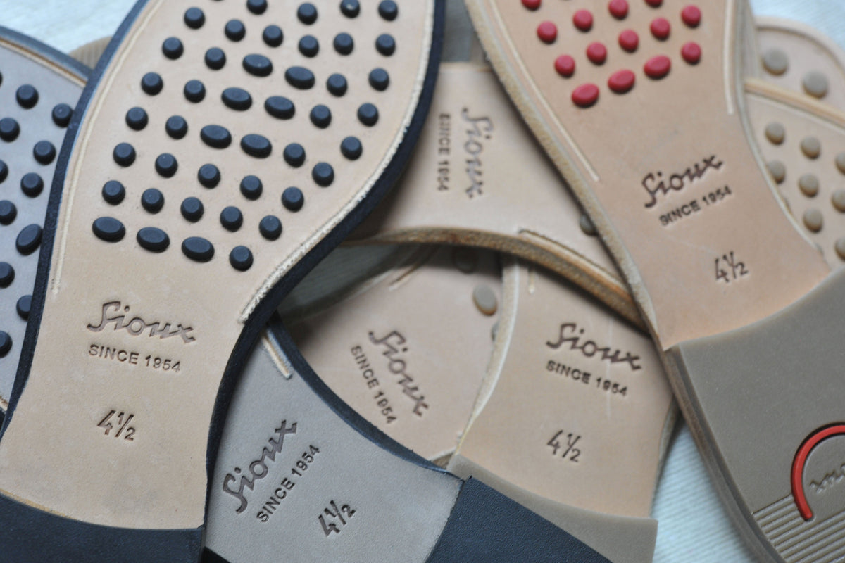 Verschiedene Sioux Schuhsohlen aus Leder mit farbigen Gumminoppen und geprägtem Sioux Logo.
