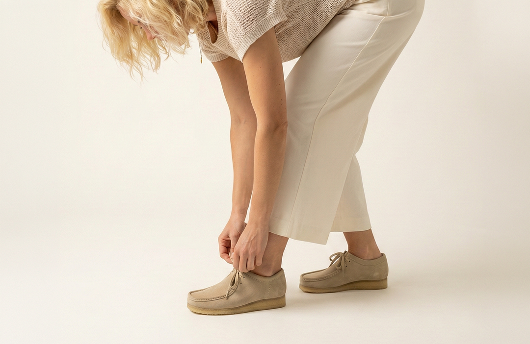 Blonde Frau bindet beige Sioux Mokassins und zeigt eine bequeme, alltagstaugliche Passform.
