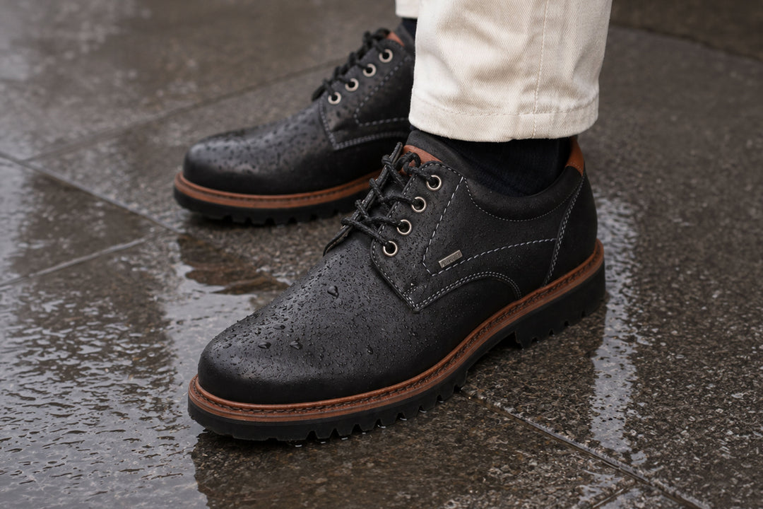 Schwarze Sioux-TEX Lederschuhe mit Wassertropfen auf nassem Untergrund als Symbol für wasserabweisenden Wetterschutz.