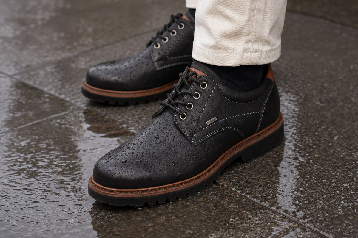 Schwarze Sioux-TEX Lederschuhe mit Wassertropfen auf nassem Untergrund als Symbol für wasserabweisenden Wetterschutz.