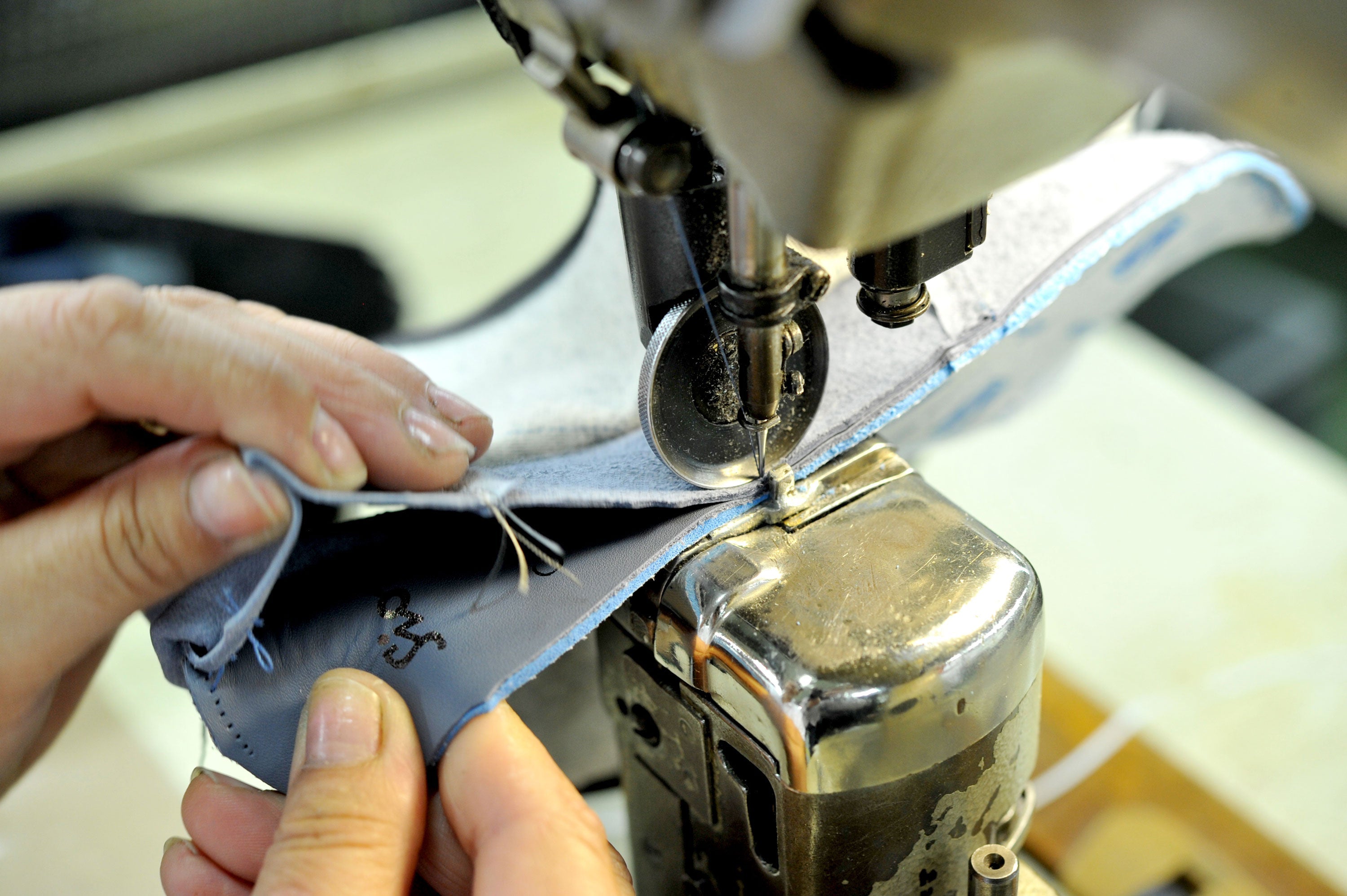 Hände führen ein Lederteil unter der Nähmaschine – präzise Verarbeitung eines Schuhschafts in der Stepperei.