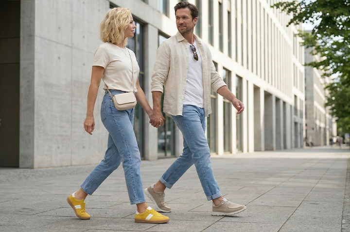 Frau und Mann gehen Hand in Hand durch eine moderne Stadt und tragen bequeme Sioux Schuhe in Gelb und Beige.